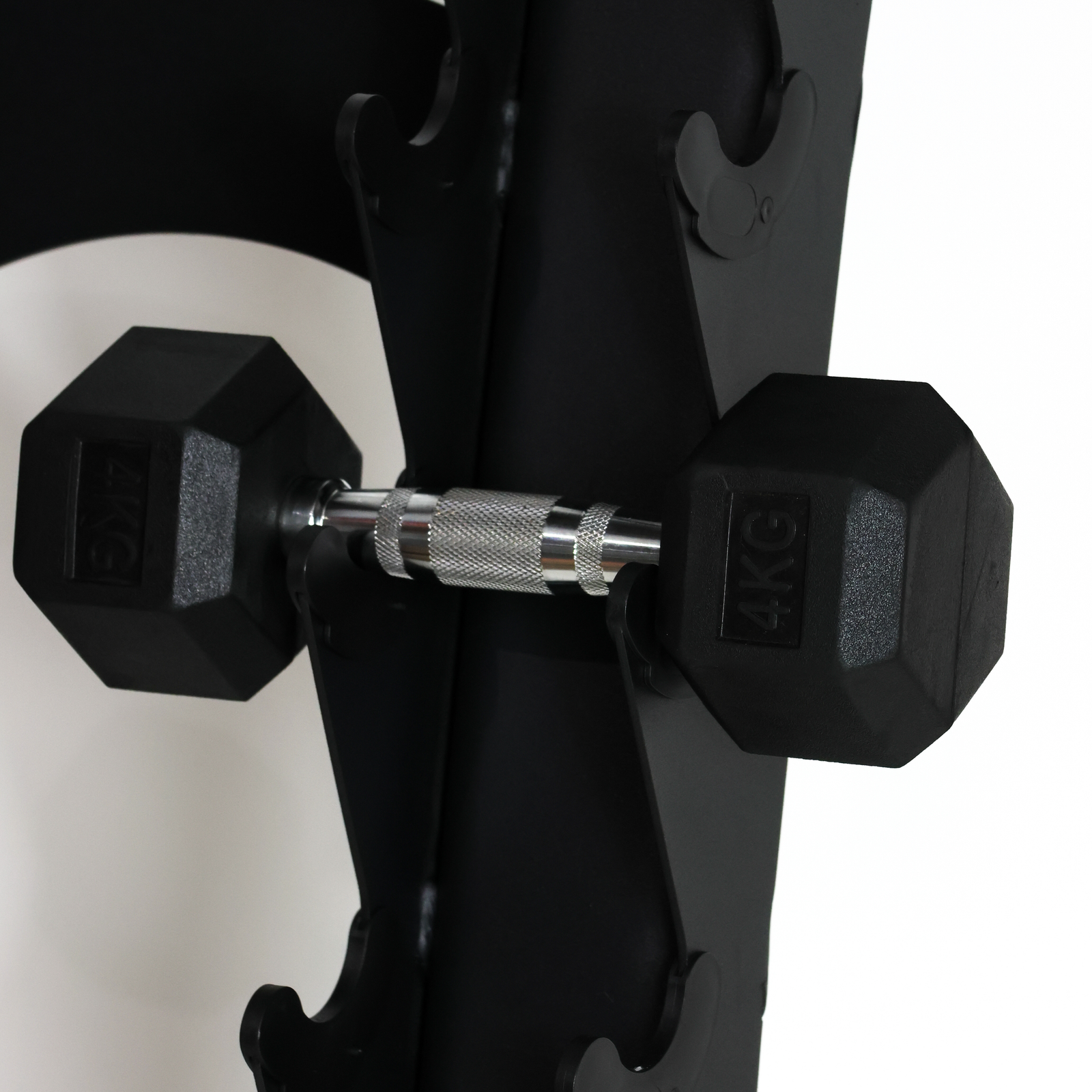 Black hex dumbbells with silver knurled handles resting on a black weight rack, with one dumbbell marked 5KG and the other marked 4KG.