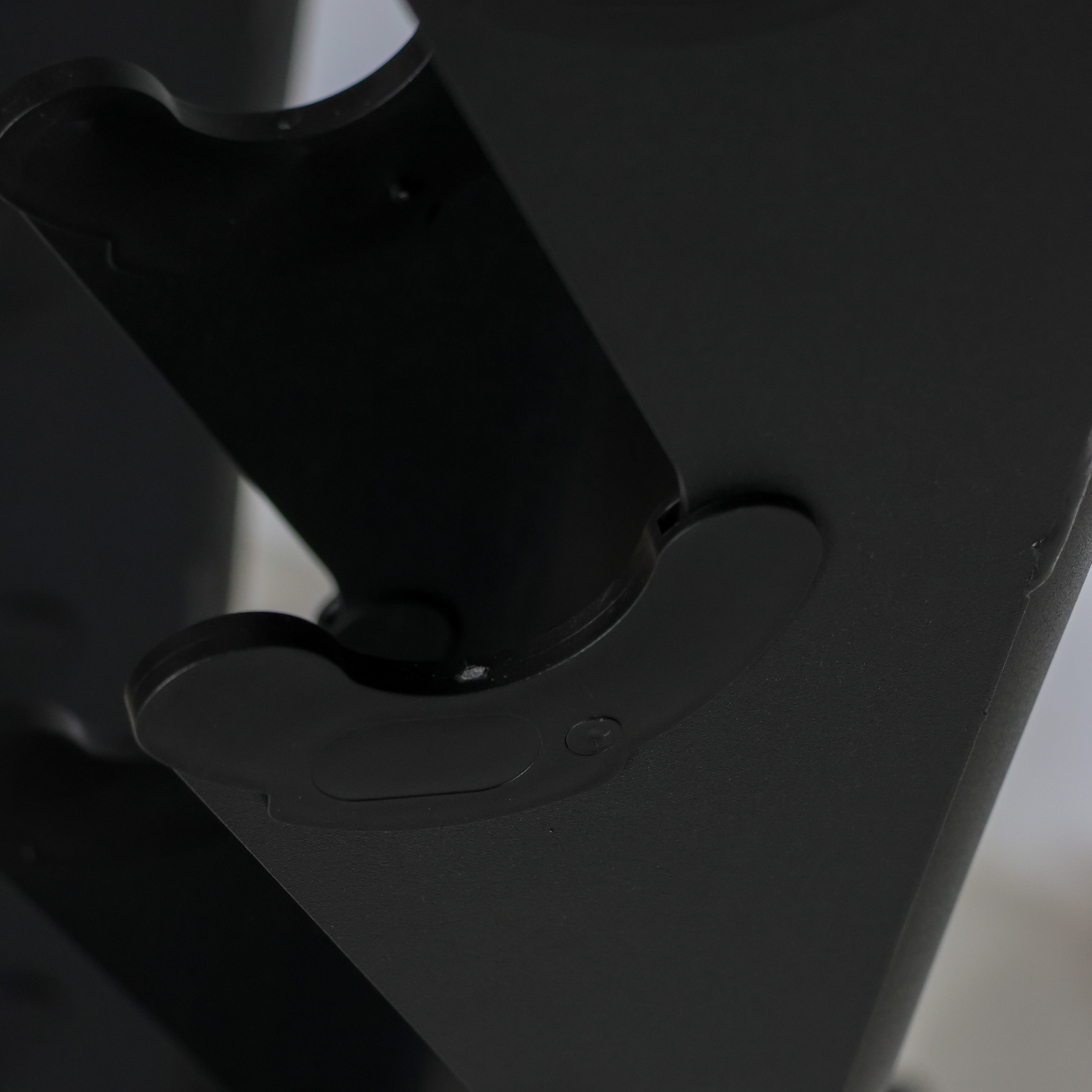 Close-up detail shot of a matte black plastic component, showing a curved mounting bracket or clip with a small circular screw detail.