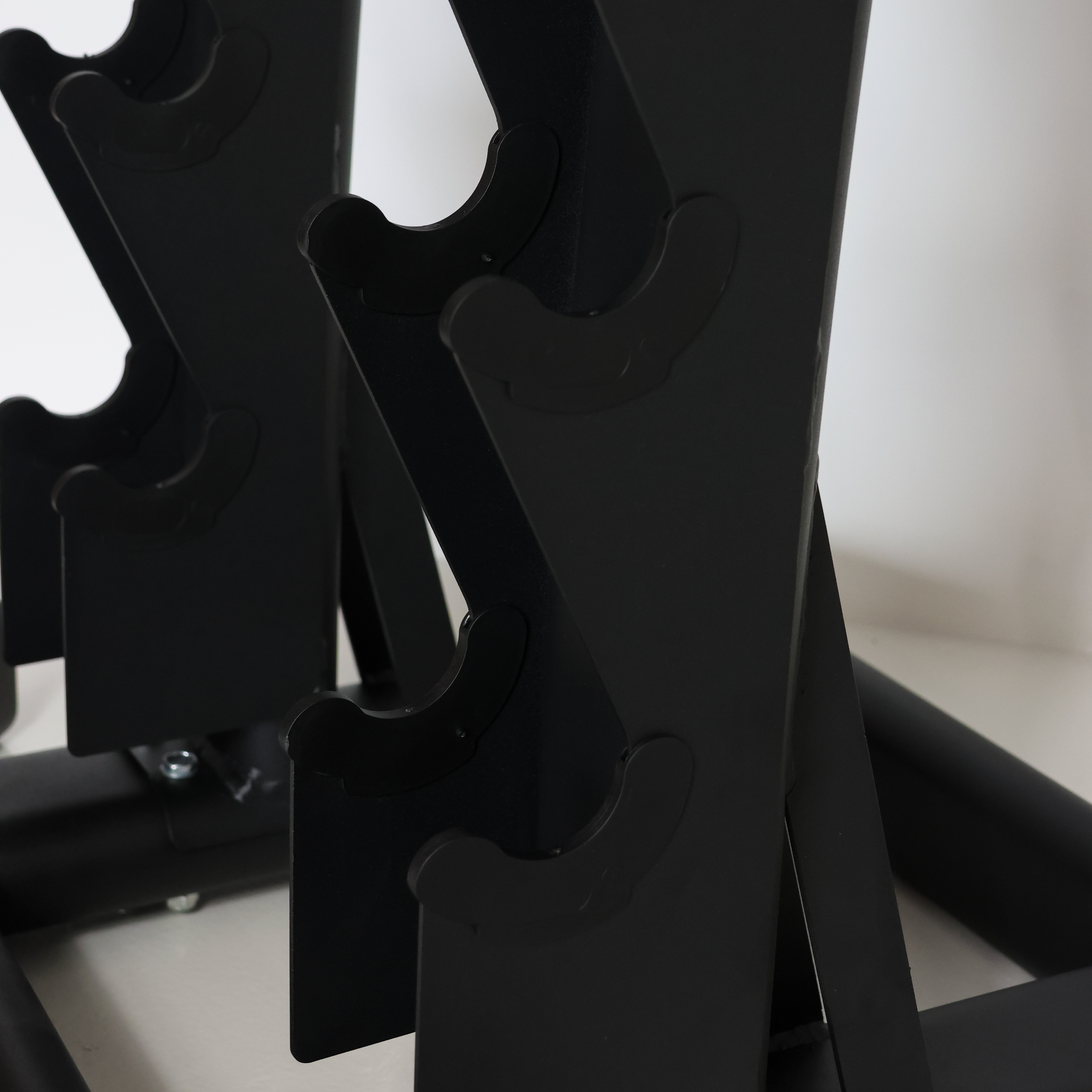 Close-up of a black metal weight rack with curved pegs holding dumbbells, set against a plain light background.
