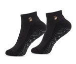 A pair of black low-cut ankle socks with a small gold, white, and black striped detail on the ribbed cuff, and a wavy gray grip pattern on the sole.